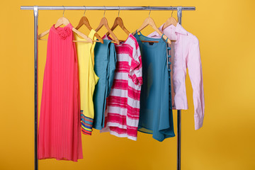colorful womens clothes on hangers on rack on orange background.