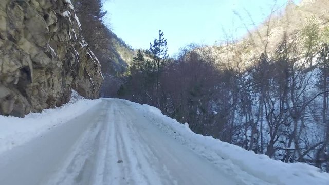 Moving on a snowy and narrow curvy mountain road near to a stream in gorge, rear wiew.