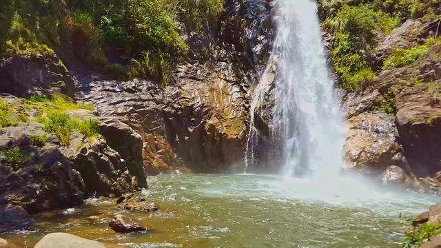 high powerful waterfall falls in deep pond among big rocks in tropical jungle