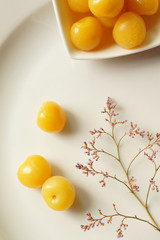canned yellow cherries on a plate and a twig with small flowers