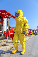 Fototapeta premium Man in yellow protective hazmat suit and fire trucks