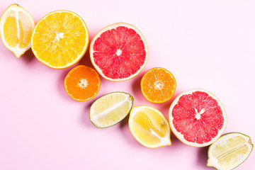 Fototapeta na wymiar Several kinds of whole and cut citrus on a pink background