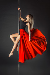 Young slim pole dance girl in red  skirt on a black studio background