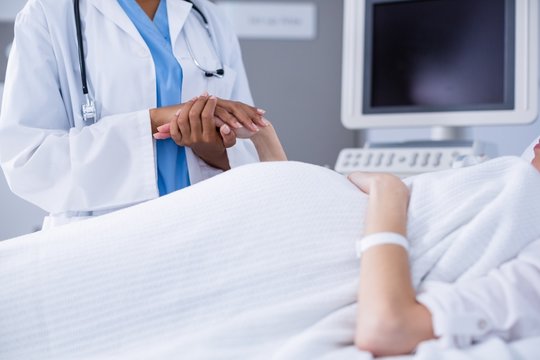 Mid section of doctor comforting pregnant woman