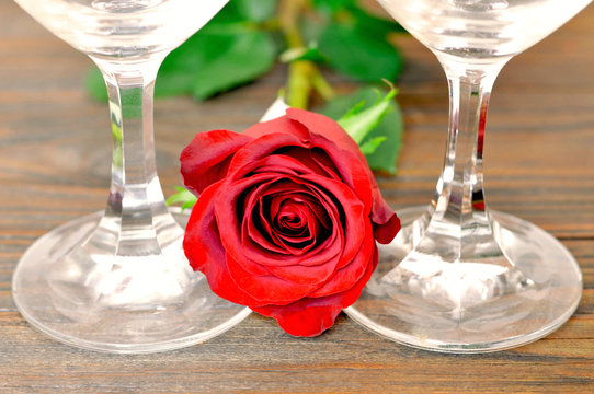 Valentines Day composition with two wine glasses and red rose on wooden background. Romantic celebration concept. 