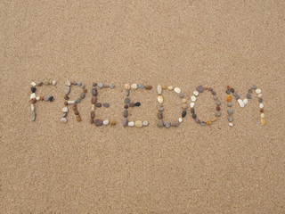 word freedom written with stones and shells on the beach by the ocean