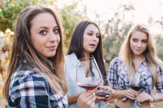 Three young female friends drinking wine in vineyard at sunset