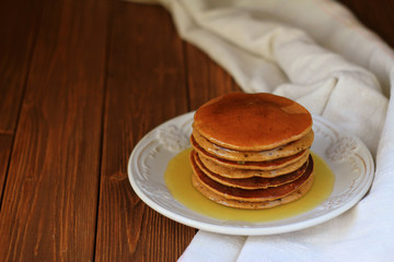  pancakes with honey on a plate on a dark wooden table with linen tablecloth