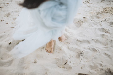 Happy bride walking barefoot on a wedding day at the beach. Nice romantic blue beautiful dress, bare feet in sand. Dress flying up in wind. Love story details. Love concept. Copy space.