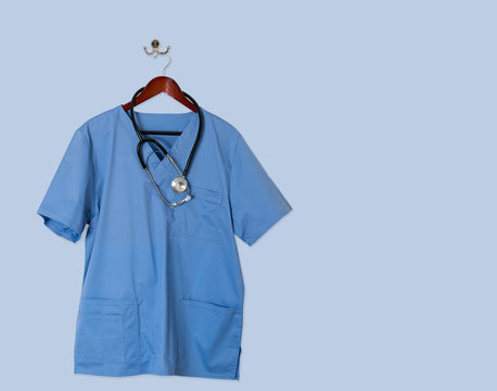 Blue scrubs shirt for medical professional hanging on blue wall