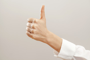 Woman hand with thumb up on gray background