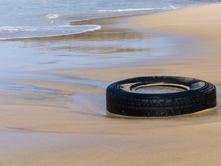 Sandy beach polluted by an old plastic tire.