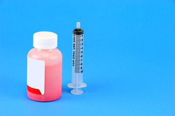 Prescription medicine bottle and oral syringe for baby isolated on blue background