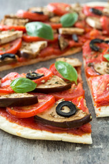 Vegetarian pizza with eggplant, tomato, black olives, oregano and basil on wooden background