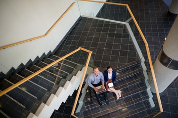 Businessman and woman sitting on steps using laptop
