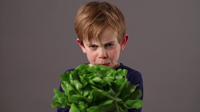 unhappy beautiful child holding a green salad expressing aversion