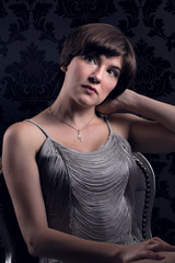 Beautiful young woman wearing silver vintage dress sat on chair.