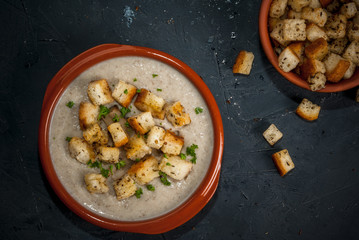 Mushroom soup with croutons and herbs, in the classic dishes for soup on a wooden table, copy space, top view