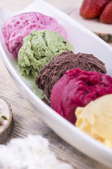 A ball of pistachio ice cream with other multi-colored balls on a light wooden background in white ware