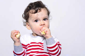 Portrait of a cute baby eating a banana.One year old kid eating fruits by himself. Adorable curly hair boy being hungry.