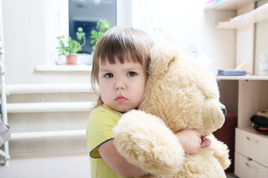 baby girl hugging teddy bear indoor in her room, devotion concept, big bear toy