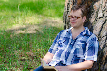 Man sits with book in hands on lawn near pine