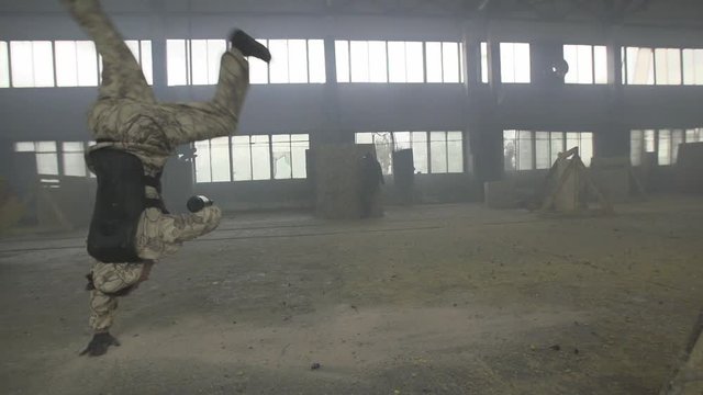 Paintball player in protective uniform and mask aiming gun before shooting. Player gets shot. Violance and war concept.