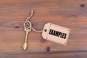Key and a note on a wooden table with text: Examples.