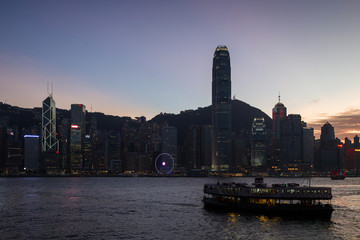 Silhouette of a Star Ferry and lit skyscrapers at the Central District on Hong Kong Island in Hong Kong, China, at dusk. Viewed from Tsim Sha Tsui, Kowloon.