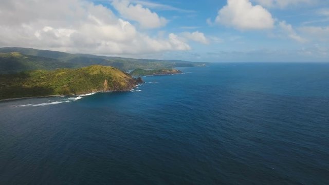 The coast of the tropical island with the mountains and the rainforest on a background of ocean with big waves.Aerial view: sea and the tropical island with rocks, beach and waves. Seascape: sky