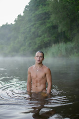 cute sexy athletic guy without underwear is standing in the river, morning, dawn