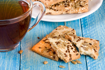 crispy bread with seeds of sunflower, flax and sesame seeds with a cup of tea on a blue wooden background
