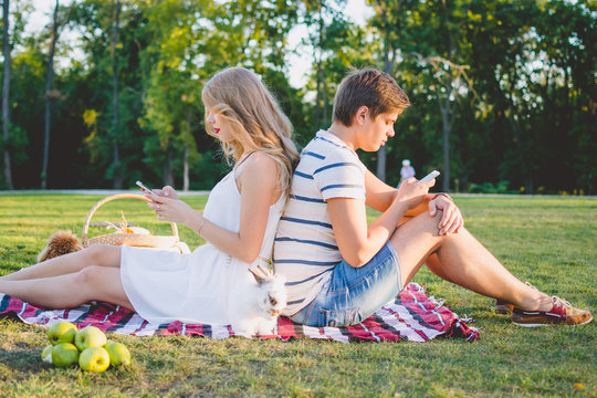 Young attractive couple resting in the park and using smarphones