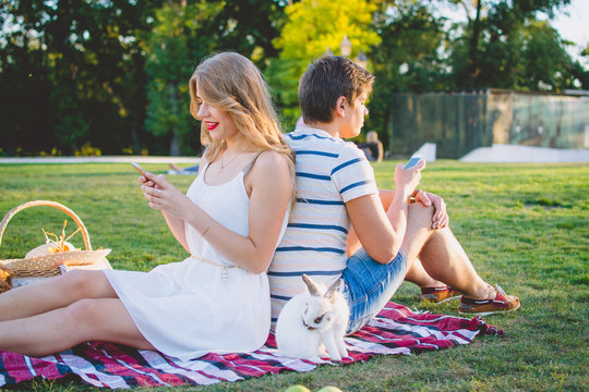 Young attractive couple resting in the park and using smarphones