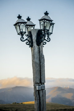 Four lampposts on a pole on a fairly high mountain, with distant mountains and low clouds on the horizon