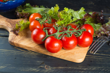Fresh red small tomatoes and green leaf salad in blue bowl ready to eat