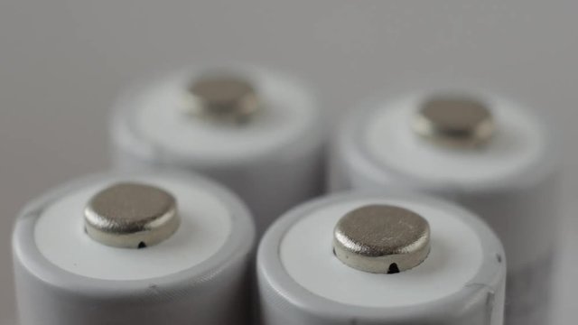 Positive terminals of four batteries slowly rotates on a white background.