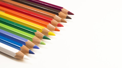 Colored pencils laying neatly in a row pointing downwards to the right on a white background