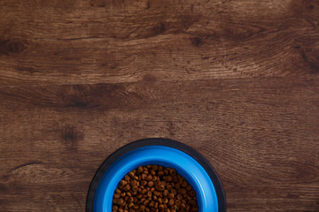 Bowl of dry kibble dog food. Healthy pets feed. Blue plate on wooden rustic background.