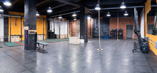 Contemporary spacious cross-fit gym with trainers, sport equipment and a rope for climbing