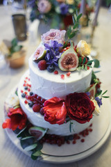 A large two-tiered cake decorated with fruit and fresh flowers. The composition of flowers, fruits and berries. Trendy wedding cake.