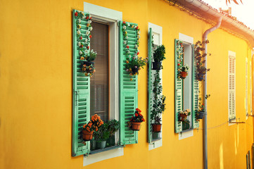 Fototapeta na wymiar Windows with beautiful floral decoration on a yellow house.Traditional mediterranean look.Sunny day