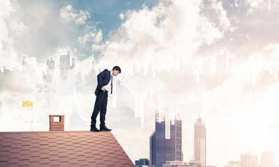 Businessman looking down from roof and modern cityscape at backg