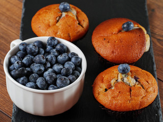 Blueberry muffins and a bowl with blueberries on a table.