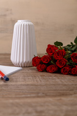 Red roses with white vase. Valentines day concept. Red pencil with notepad. Love design. Wooden rustic board.