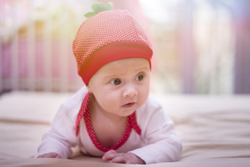 Happy baby wearing strawberry shirt and pants. Newborn child relaxing in bed. Close up of a beautiful baby girl lying on the bed. Lens flare in the background.