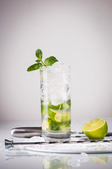 Glass of mojito cocktail with knife, half of a lime and ice on t
