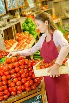 Shop assistant restocking pile of tomatoes