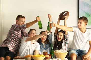 Young fans watching rugby match on TV with beer and snacks