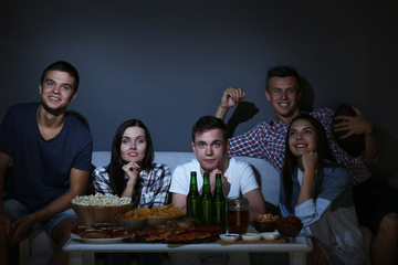 Young fans watching sports on TV late in evening with beer and snacks